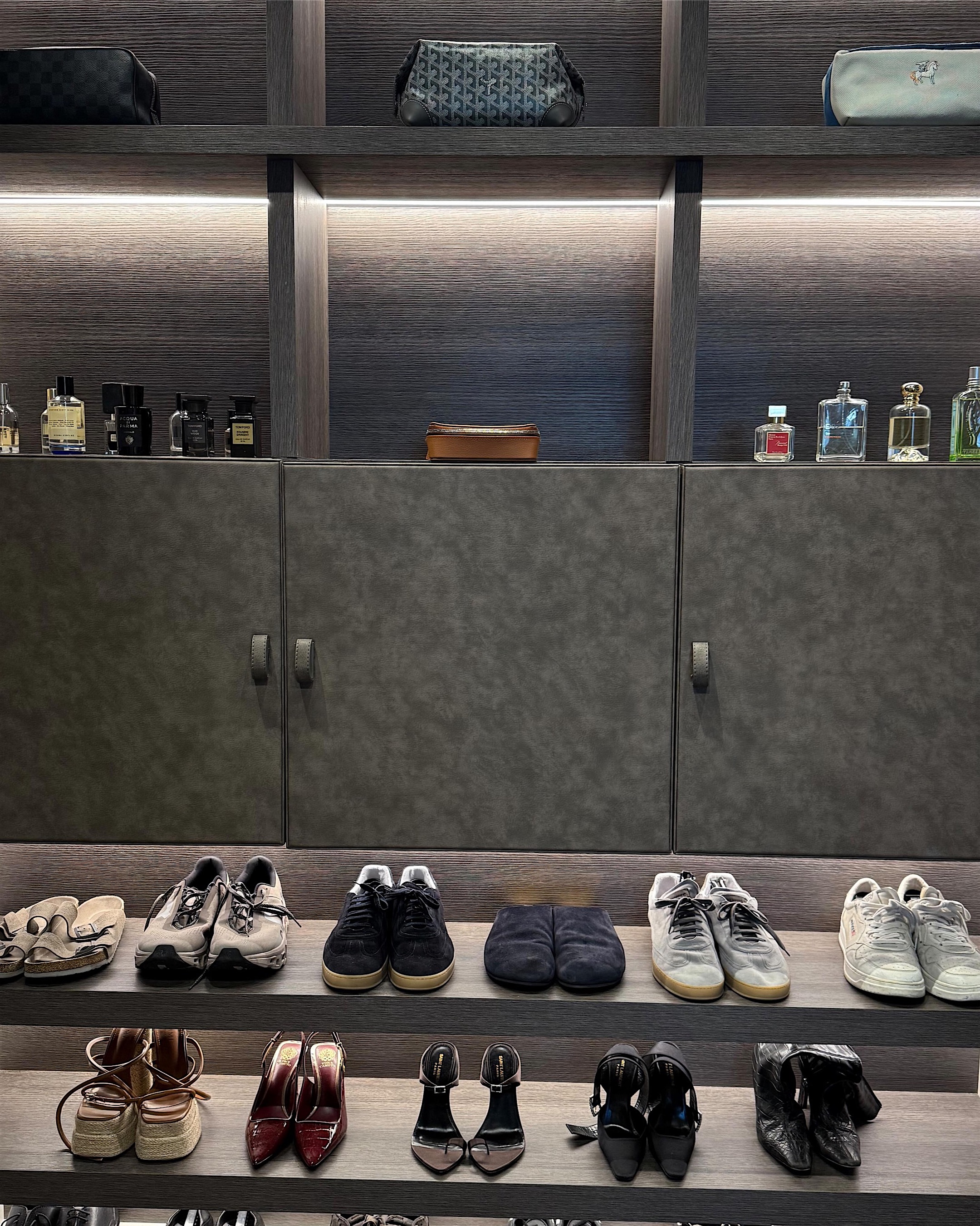 A lit wall of shoes and fragrance on dark shelving, every pair spaced and facing forward