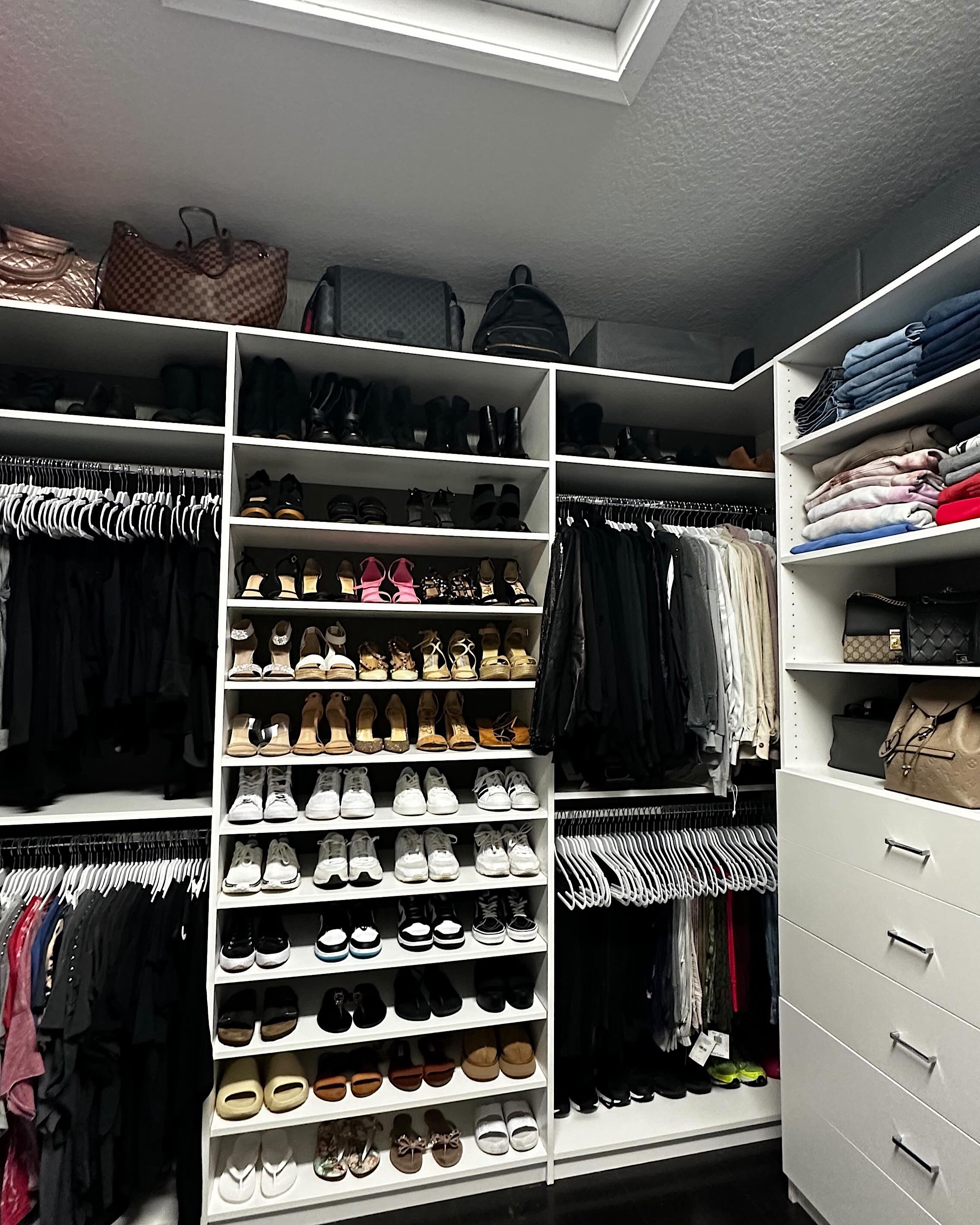 A white walk-in closet with shoes in rows and hanging in categories