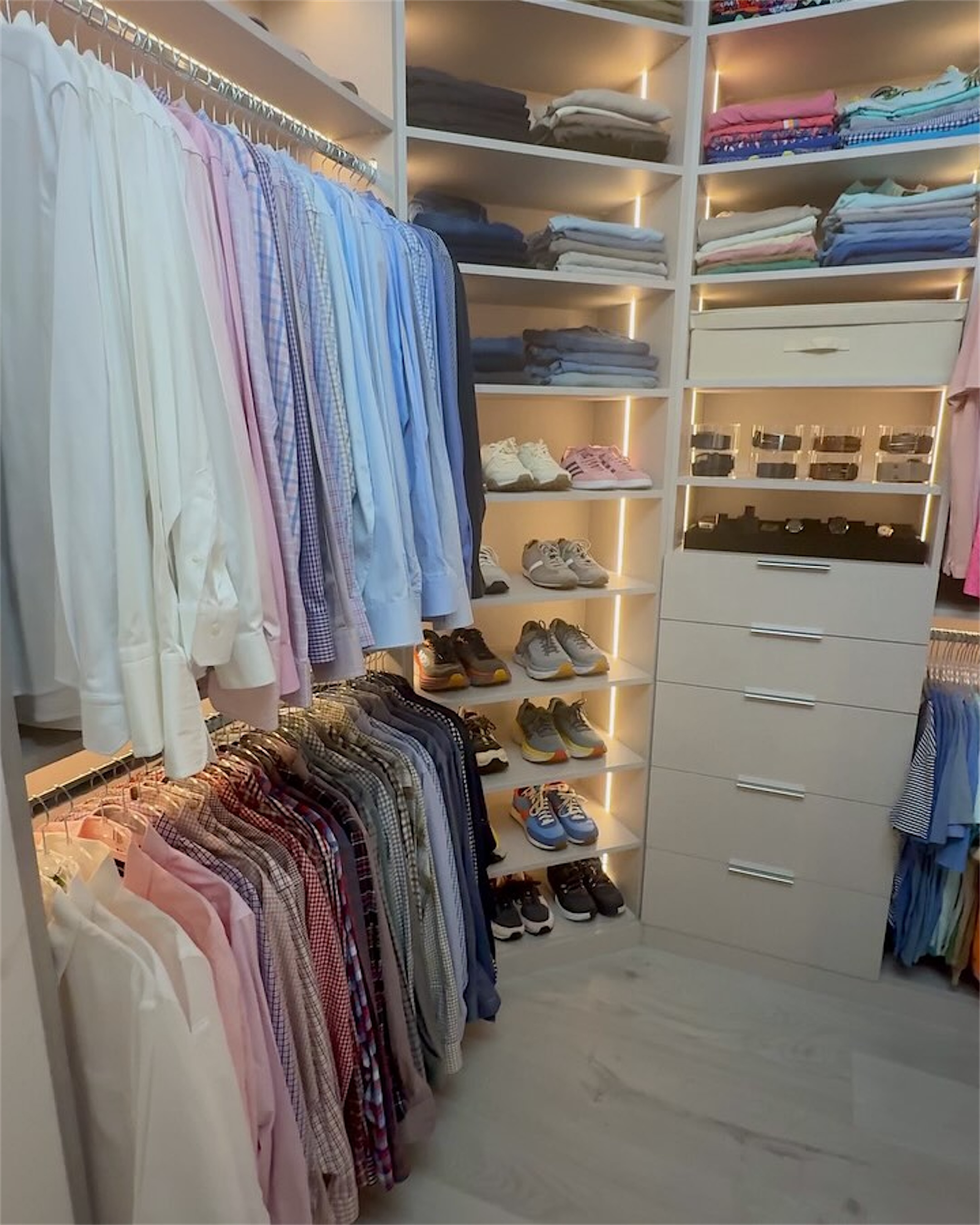 A softly lit dressing room with shirts hanging by color and shoes on shelves
