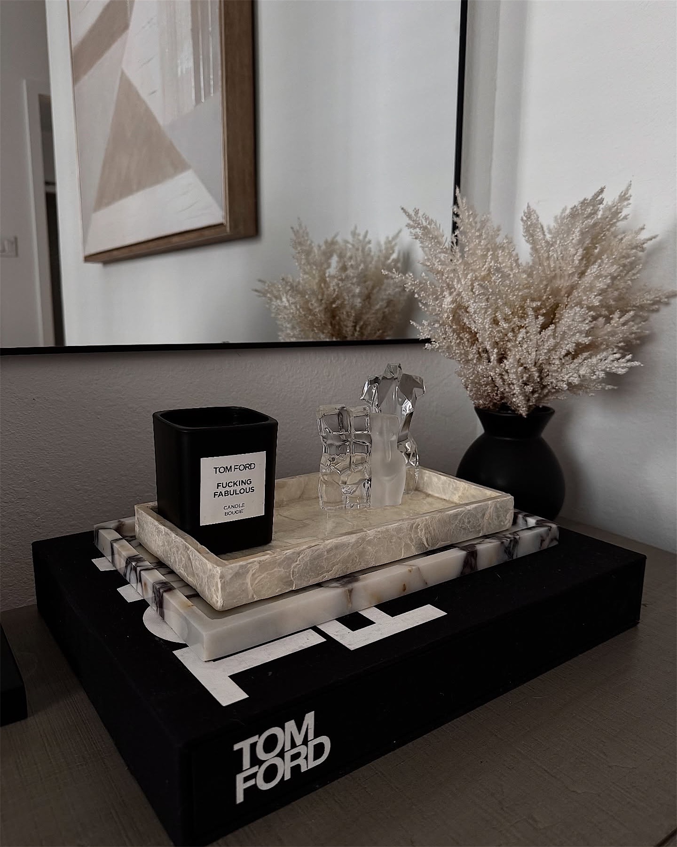 A styled tray with a candle, glassware and dried grasses